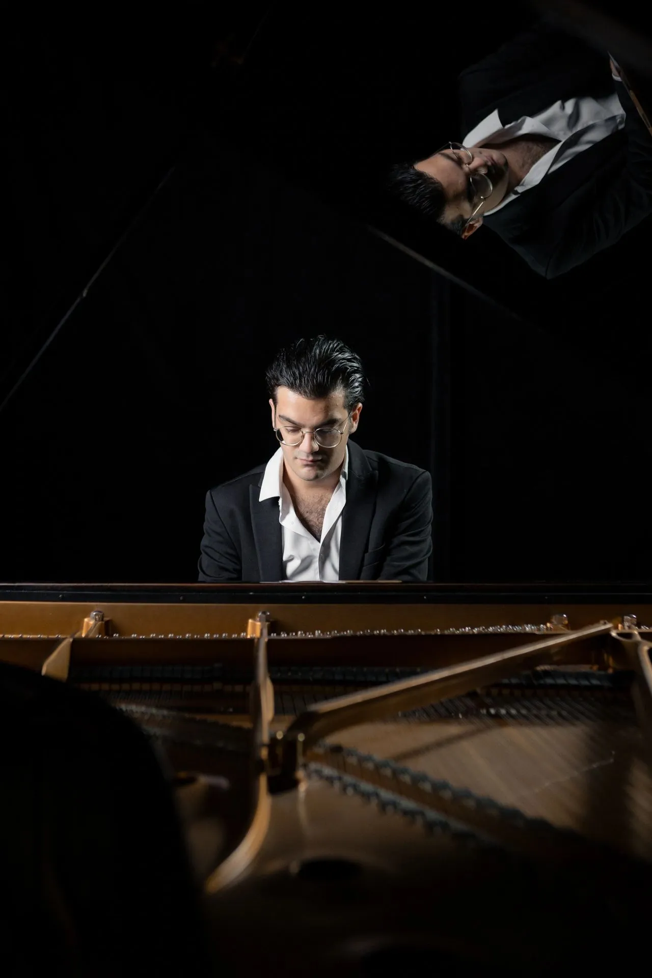 Sandro Nebieridze al pianoforte, il volto riflesso nel coperchio sollevato dello strumento
